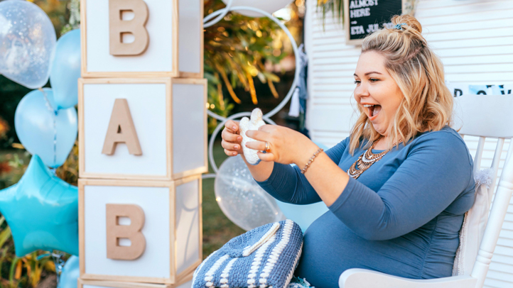 A pregnant woman at her baby shower smiling as she opens a gift