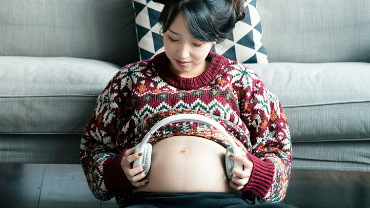 fetal hearing, pregnant woman holding headphones over her bump