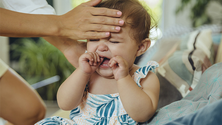 teething fever, older baby with a fever and hand in her mouth