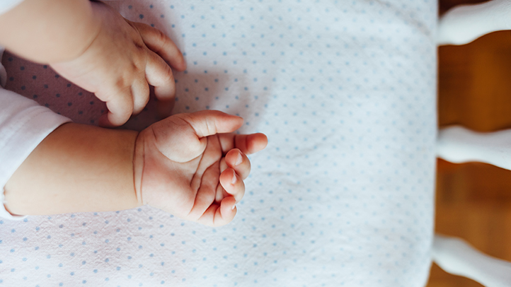 when can babies sleep on their stomachs, baby's hands in crib